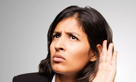 Foto einer Frau, die ihre Hand ans Ohr hält, weil sie schlecht hört