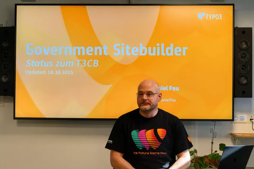 Daniel Fau (CEO TYPO3 GmbH) hält auf dem TYPO3 Camp Berlin 2025 einen Vortrag. Im Hintergrund die Leinwand mit der Startfolie "Goverment Sitebuilder Status zu T3CB (Updated: 18.10.2025)
